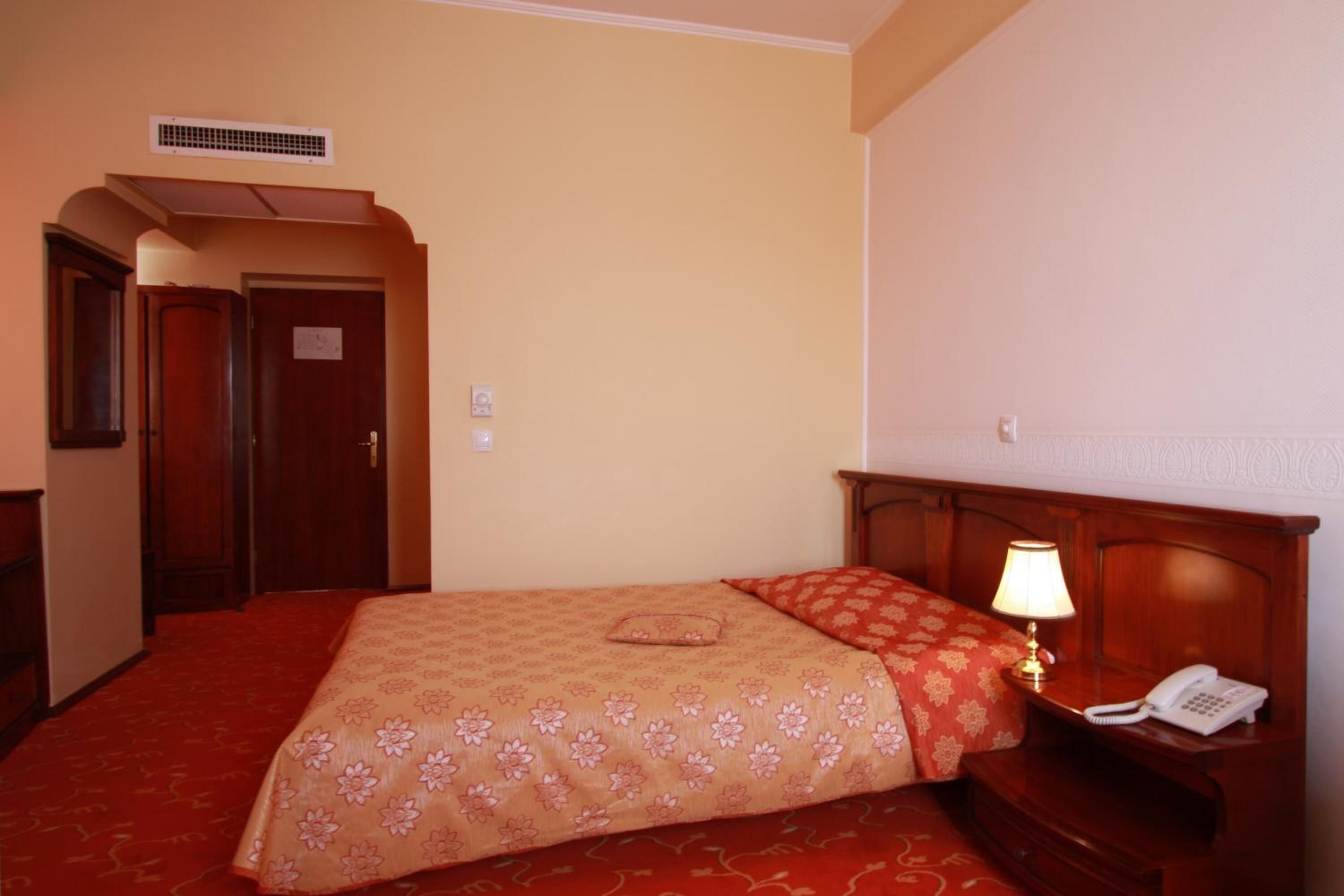 Una habitación de hotel con una cama, una mesita de noche con lámpara, un teléfono y una puerta.