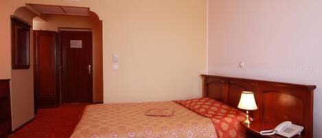 Una habitación de hotel con una cama, una mesita de noche con lámpara, un teléfono y una puerta.