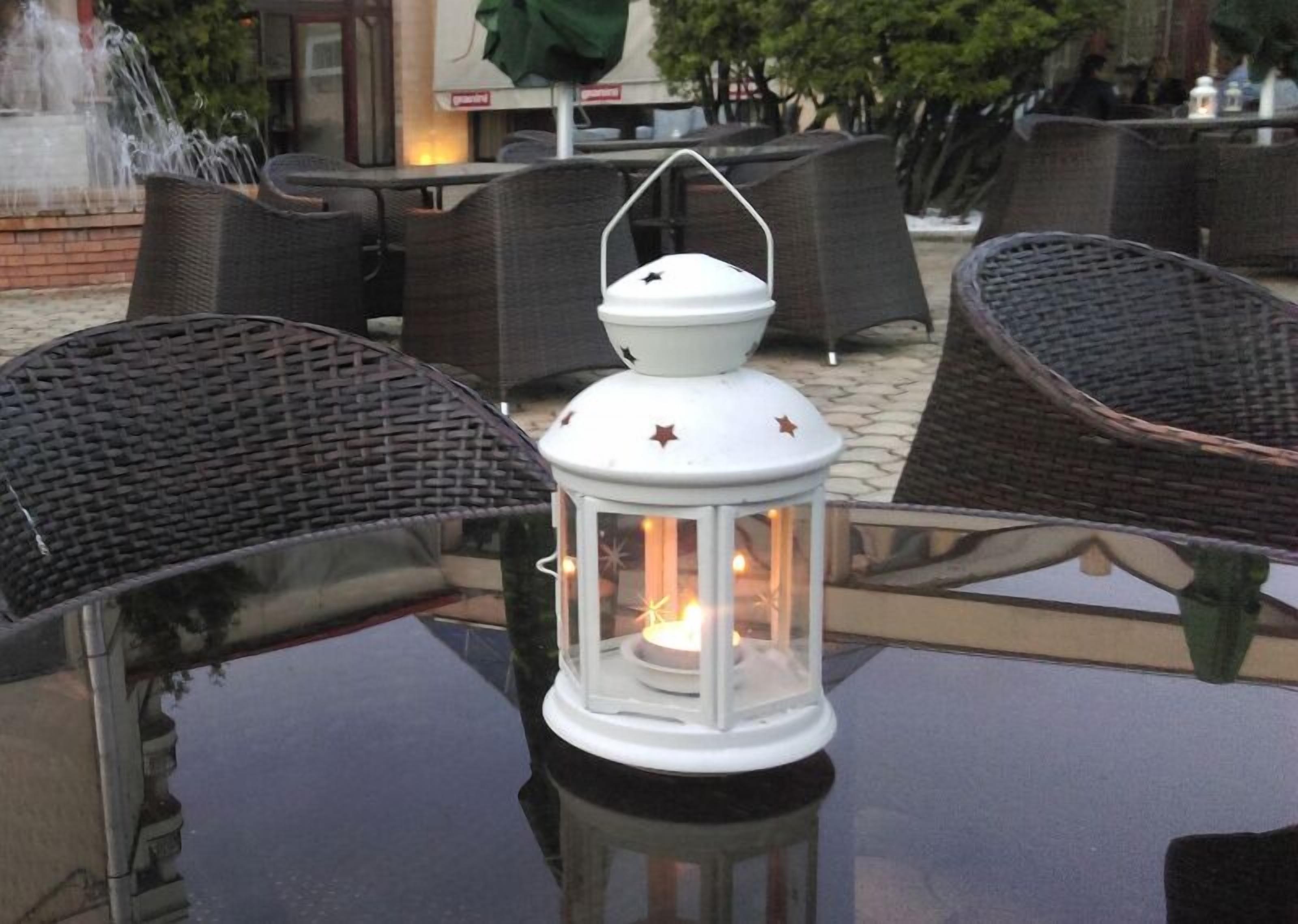 A table with a white lantern, wicker chairs, and a fountain in the background.