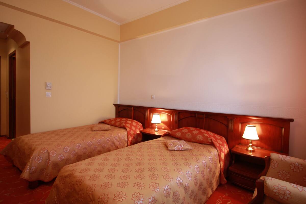 Hotellihuone, jossa on kaksi erillistä sänkyä, puiset päätyosat, yöpöydät lampuineen ja punainen matto.