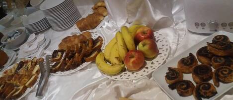 Una mesa de buffet con diversos alimentos, entre ellos plátanos, manzanas, pasteles y un tostador.