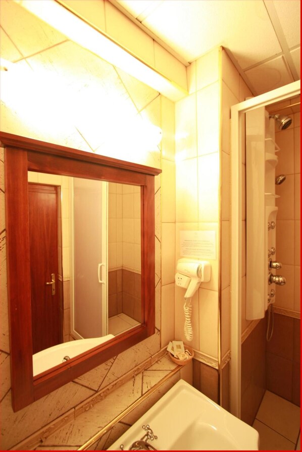 A bathroom with a wooden-framed mirror, a white sink, a hairdryer, and a shower area. - Hotel Mara (Baia Mare)