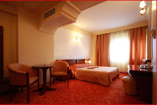 A hotel room with a bed, two armchairs, a small table, a desk, and a mirror. - Hotel Mara (Baia Mare)