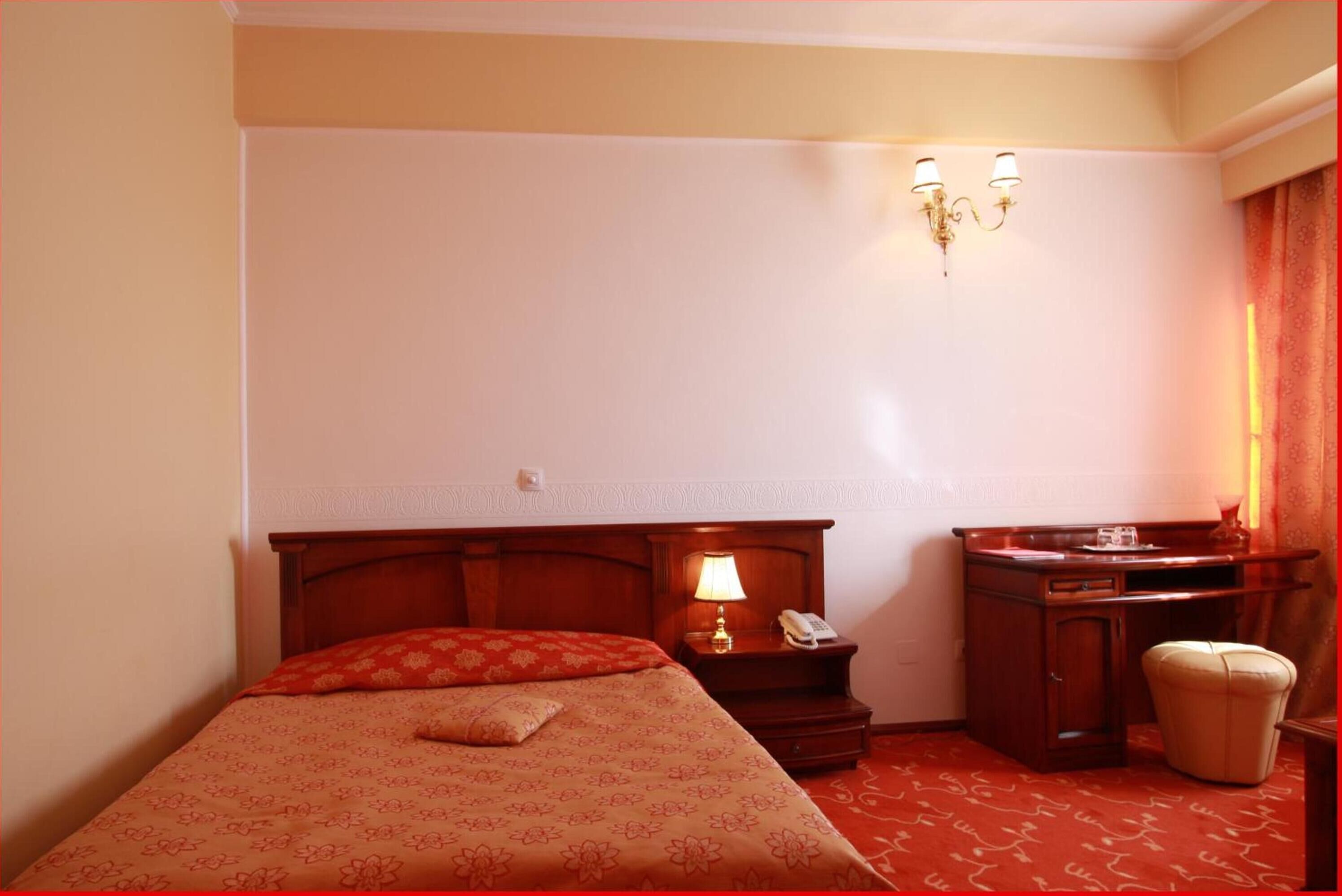 Een hotelkamer met een bed, nachtkastje met een lamp, telefoon, klein kastje en een stoel.