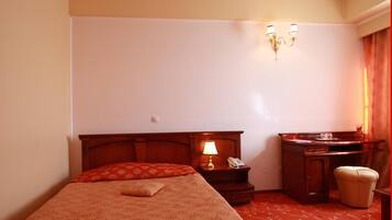 Een hotelkamer met een bed, nachtkastje met een lamp, telefoon, klein kastje en een stoel.