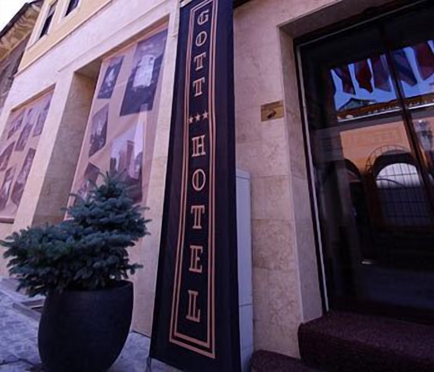 Entrada de un hotel con un letrero vertical que dice "HOTEL" y una planta en maceta a la izquierda.