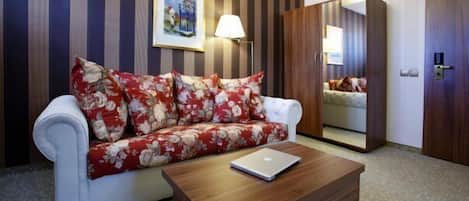 Habitación de hotel con pared a rayas, un sofá con cojines estampados, una mesa de centro de madera, un espejo y una puerta.