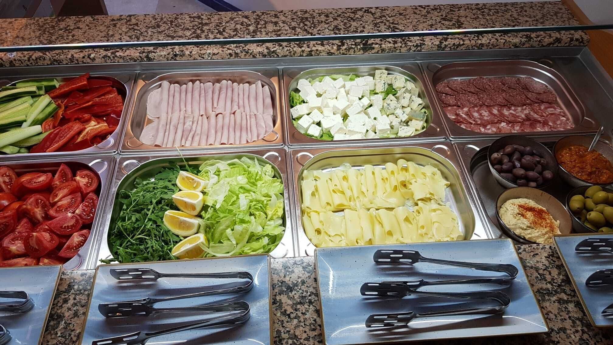 A buffet with various food items including sliced cucumbers, tomatoes, lettuce, cheese, and olives.