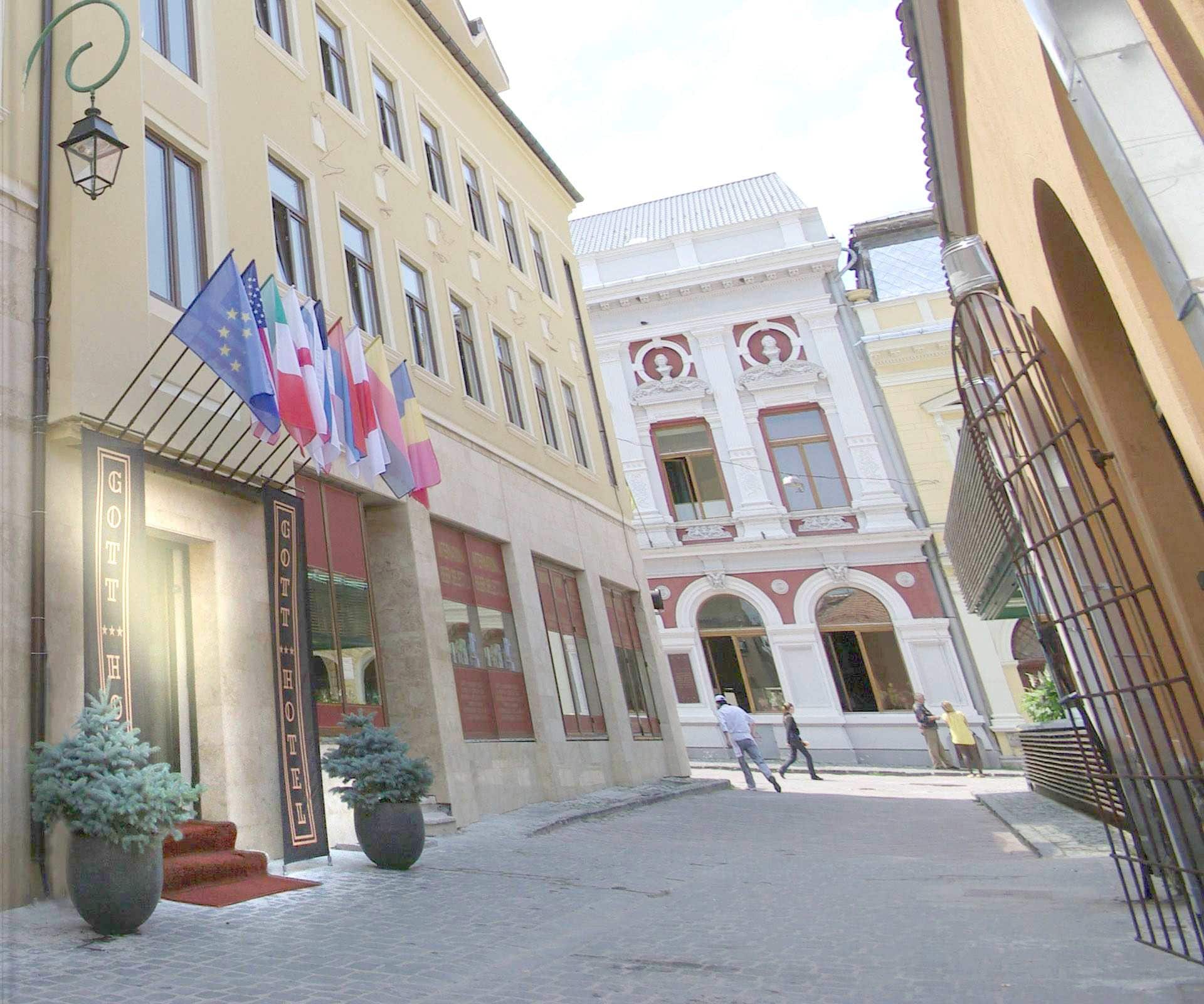 A hotel with a classic facade, multiple flags, and a cobblestone street.