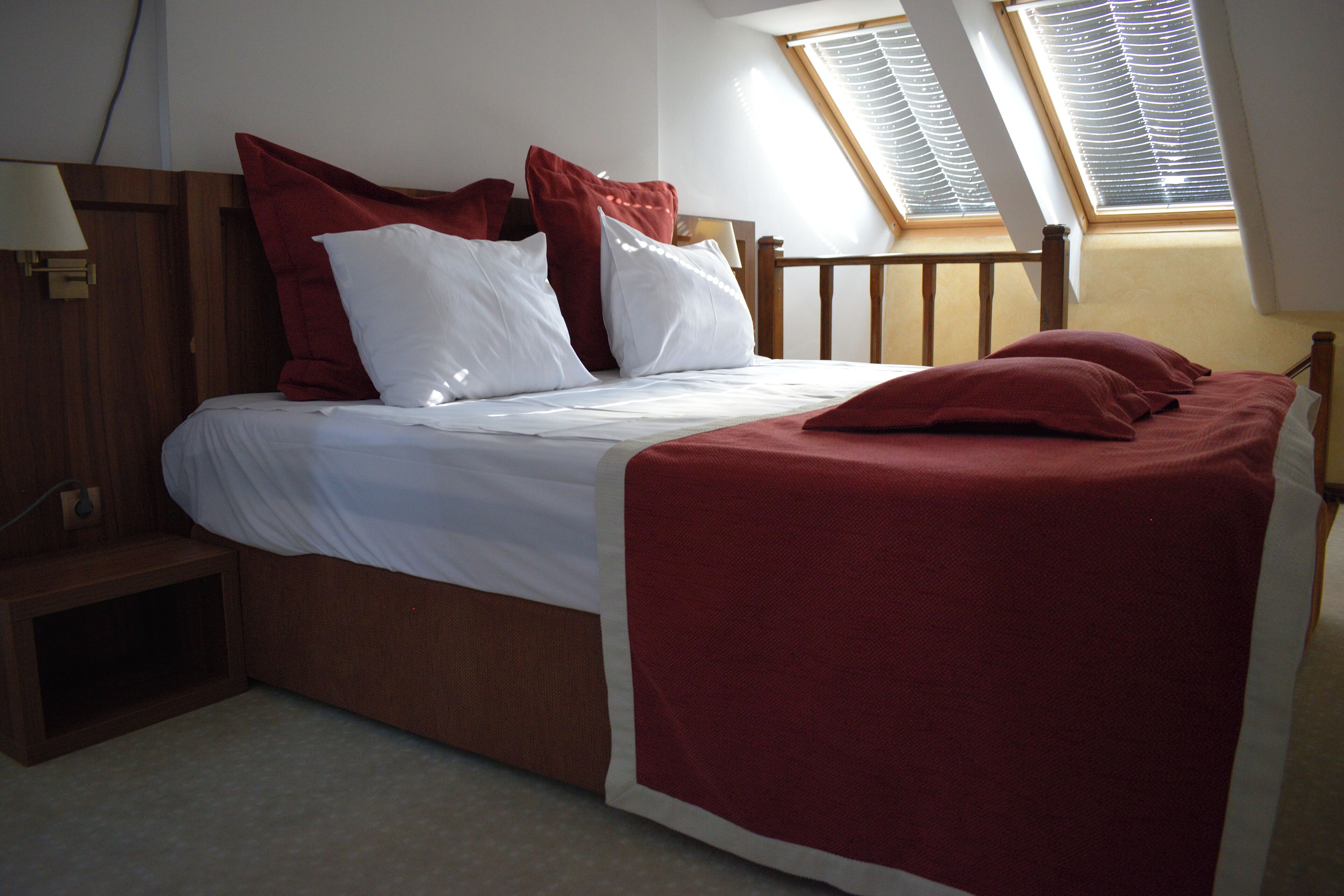 A neatly made bed with white and red bedding, a wooden headboard, and a bedside table with a lamp.