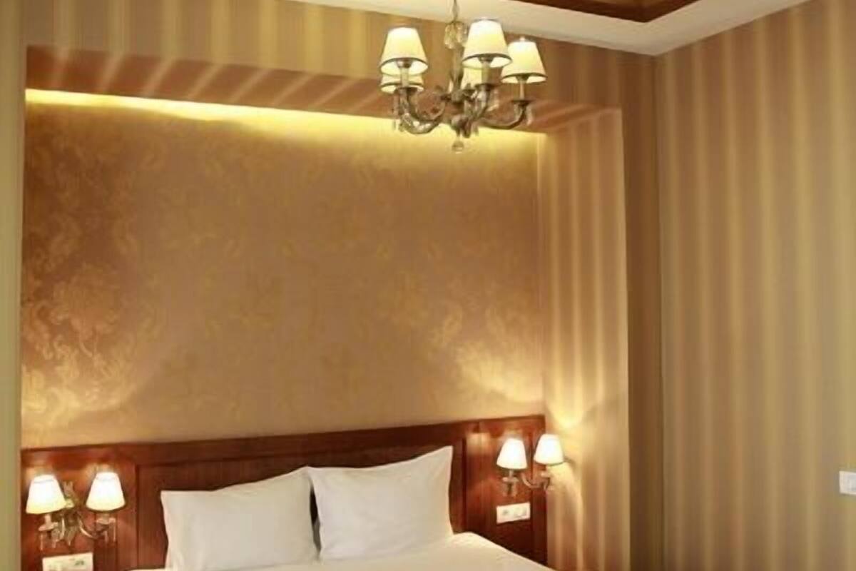 A hotel room with a large bed, a chandelier, wall sconces, and a wooden ceiling.