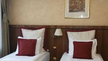 A hotel room with two beds, each with white bedding and red pillows, a nightstand with a lamp, and a framed artwork on the wall.