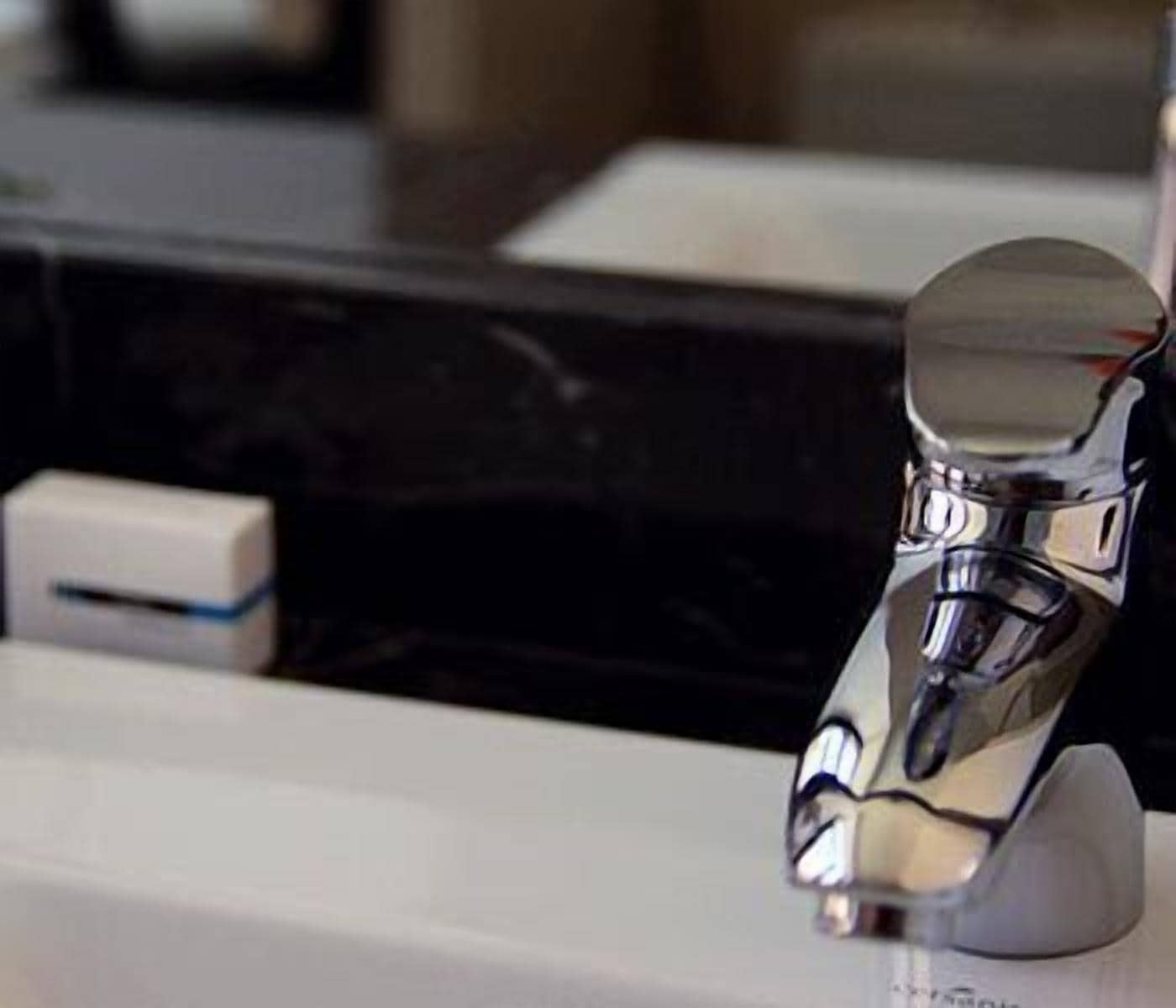 Un robinet chromé fixé sur un comptoir blanc, avec un pare-éclaboussures noir.