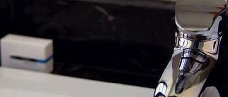 Un robinet chromé fixé sur un comptoir blanc, avec un pare-éclaboussures noir.