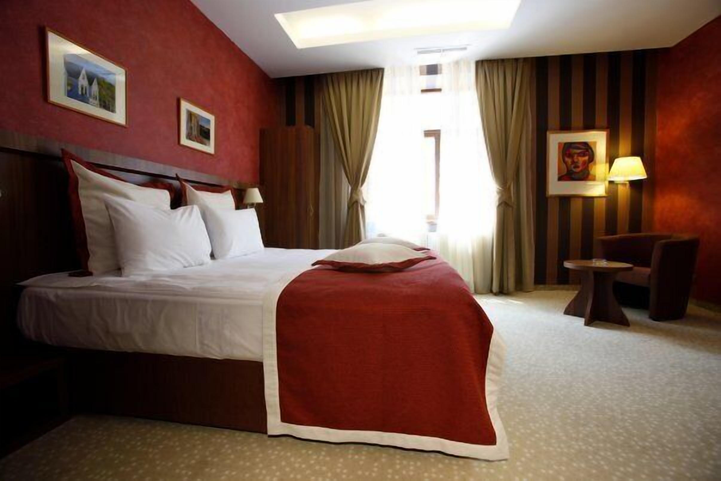 Una habitación de hotel con una cama grande, una manta roja, un escritorio y una silla.