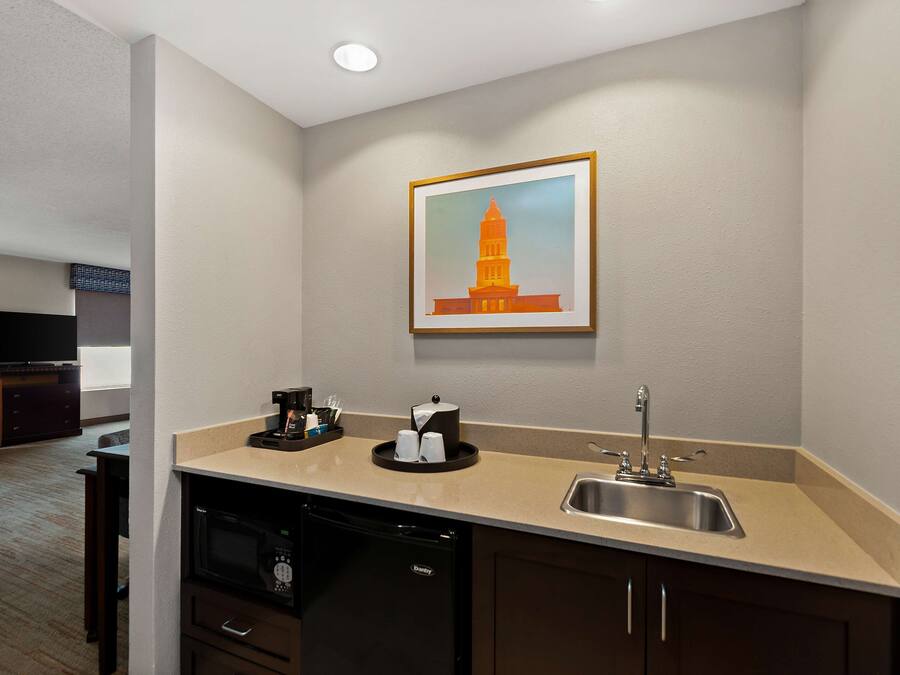 A hotel room with a kitchenette, a sink, a microwave, a coffee maker, and a framed picture of a tower on the wall.