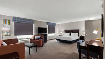 A hotel room with a bed, a desk, a chair, a TV, and a window with blinds.