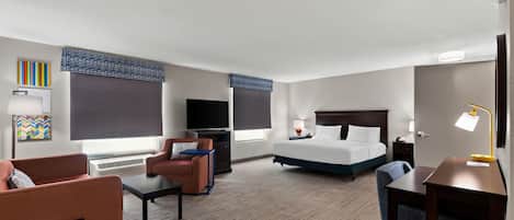 Ein Hotelzimmer mit Bett, Schreibtisch, Stuhl, Fernseher und einem Fenster mit Jalousien.