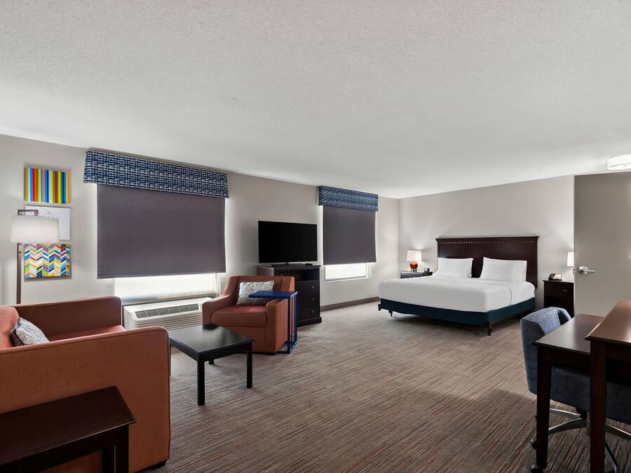 Ein Hotelzimmer mit Bett, Schreibtisch, Stuhl, Fernseher und einem Fenster mit Jalousien.