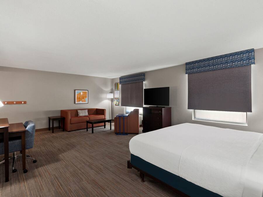 Une chambre d’hôtel équipée d’un lit, d’un bureau, d’un canapé, d’une télévision et d’une fenêtre avec des stores.
