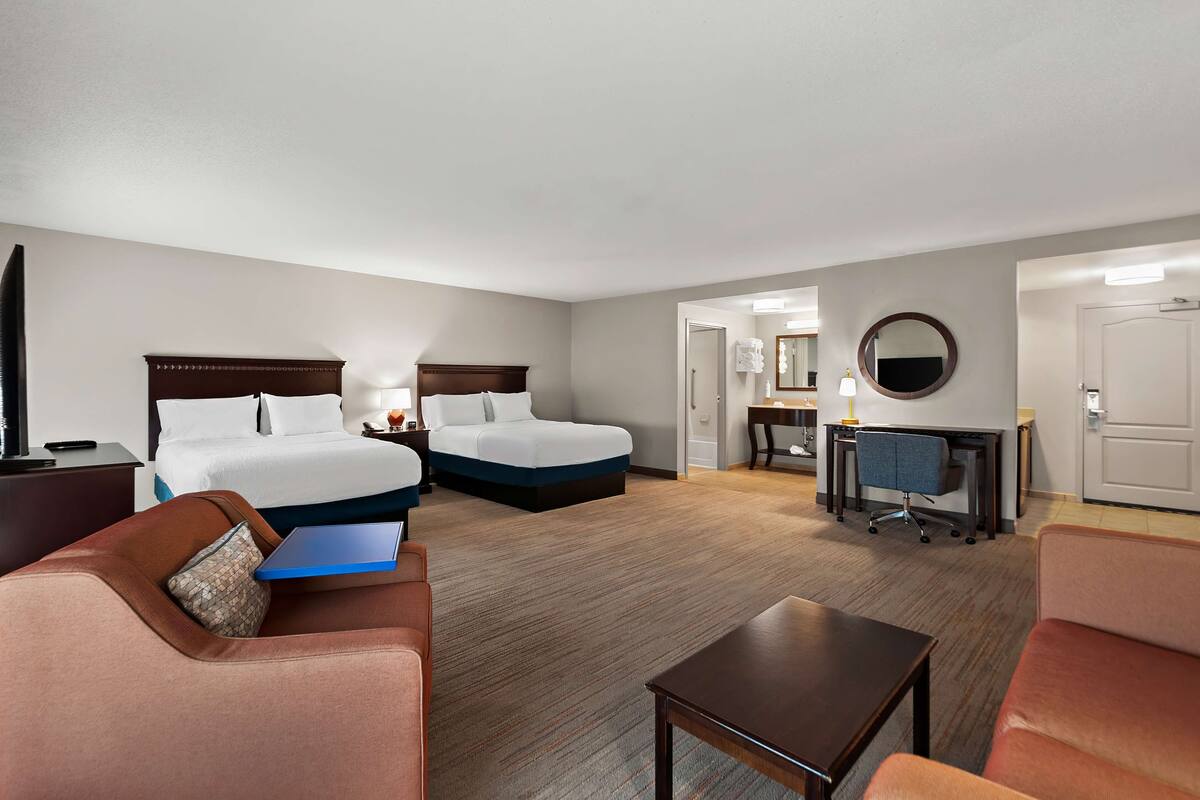 Ein Hotelzimmer mit zwei Betten, einem Schreibtisch, einem Stuhl, einem kleinen Tisch und einem Sofa.