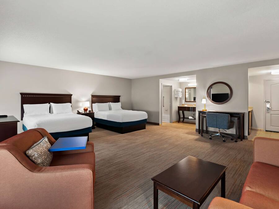 A hotel room with two beds, a desk, a chair, a small table, and a sofa.
