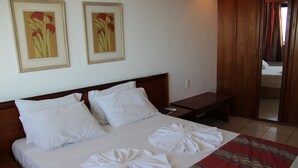 Una cama bien tendida con sábanas y toallas blancas, un cabecero de madera y dos cuadros con motivos florales en la pared.