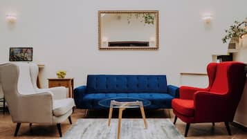 Una sala de estar con un sofá azul, un sillón rojo, un sillón color beige, una mesa de centro de vidrio y una mesita auxiliar con una planta.