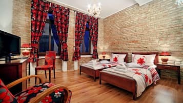 A bedroom with a brick wall, two beds, a TV, and a chandelier.