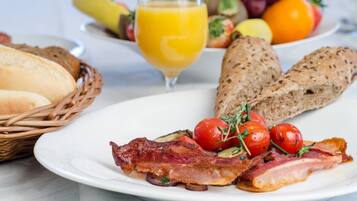A breakfast plate with bacon, tomatoes, and bread, along with a glass of orange juice and a basket of bread.