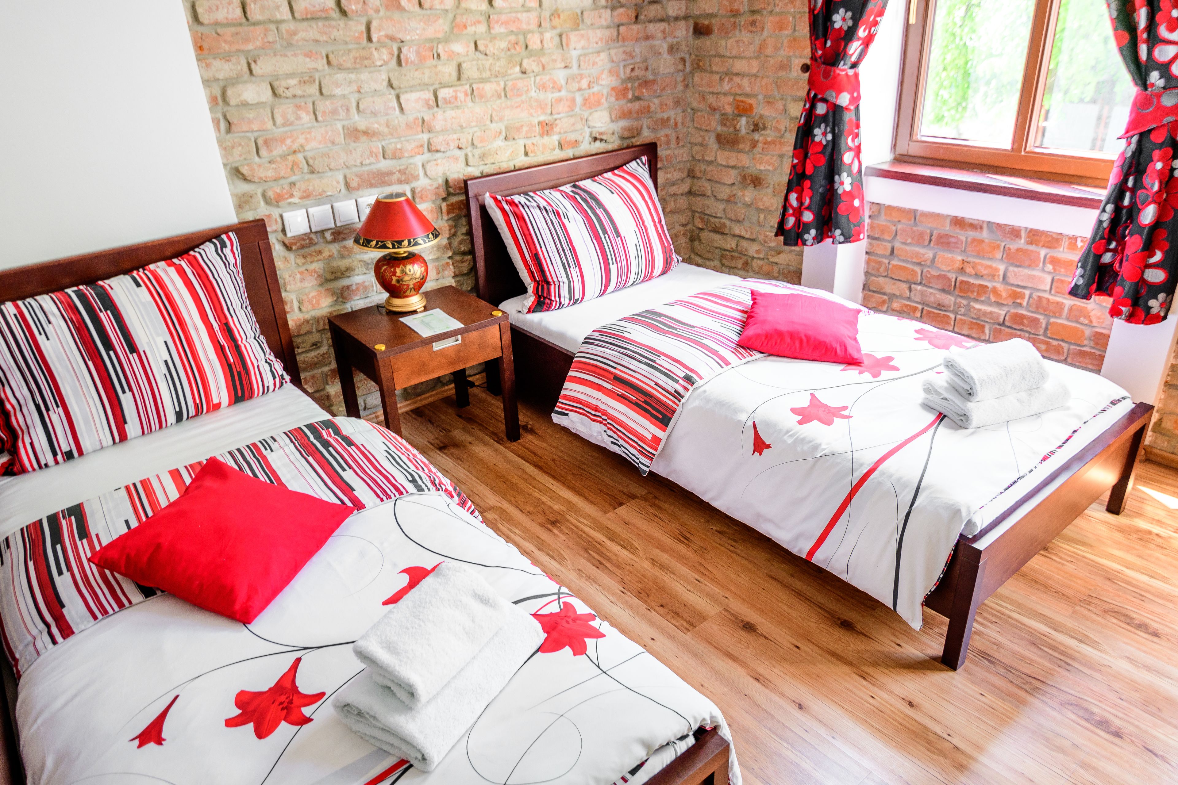 Una habitación con dos camas, una mesita de noche, una lámpara y una pared de ladrillo.