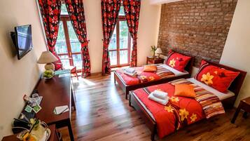 A hotel room with two beds, a wooden desk, a TV, and a brick wall.