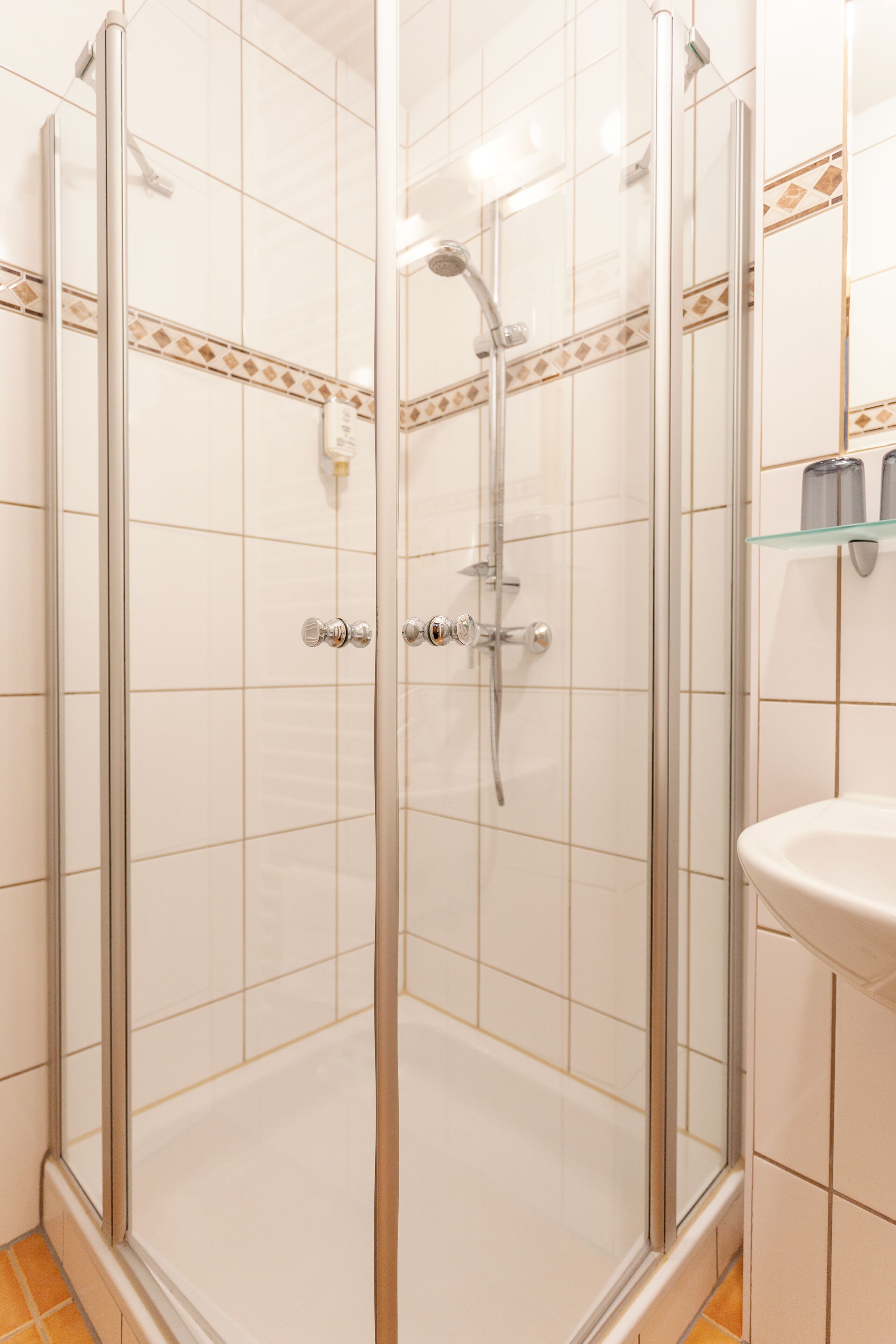 A glass-enclosed shower with a handheld showerhead and a wall-mounted faucet.