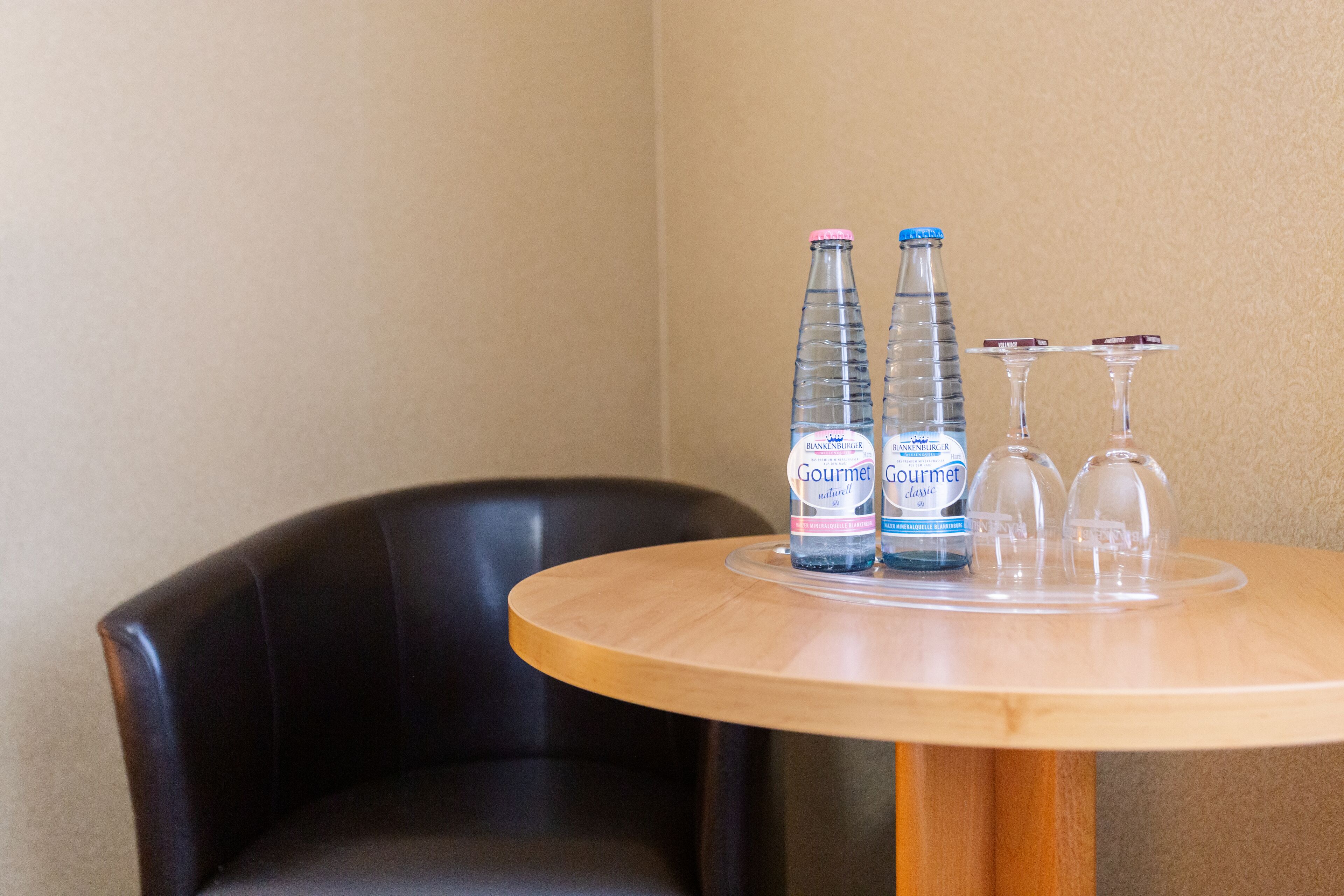 Une table ronde en bois, sur laquelle sont posées deux bouteilles d’eau et deux verres à vin.