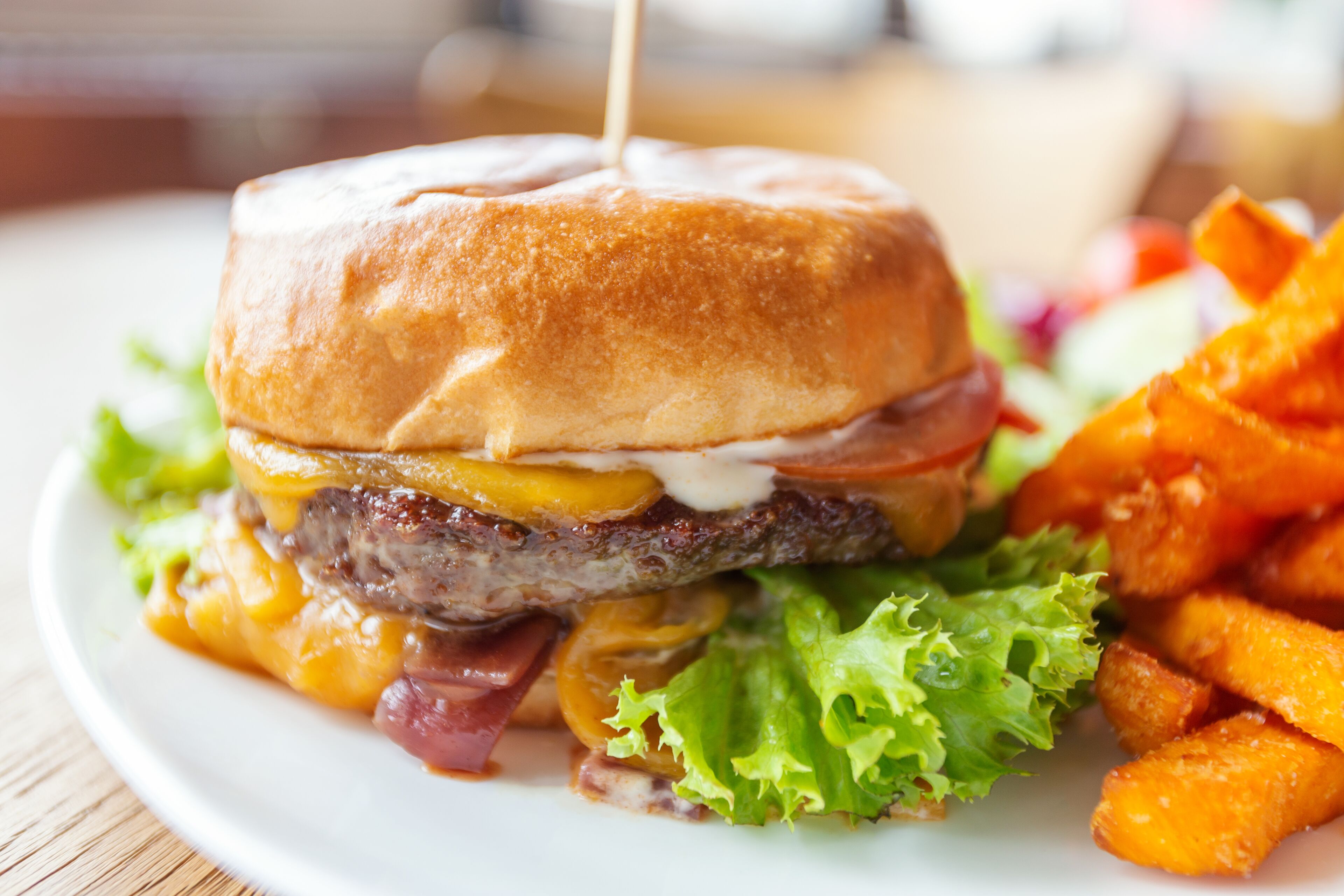 Una hamburguesa con pan tostado, queso, lechuga y una hamburguesa de carne, acompañada de papas fritas y una ensalada.