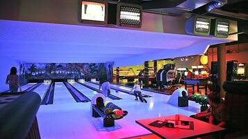 A bowling alley with multiple lanes, a mural on the wall, and a few people playing.