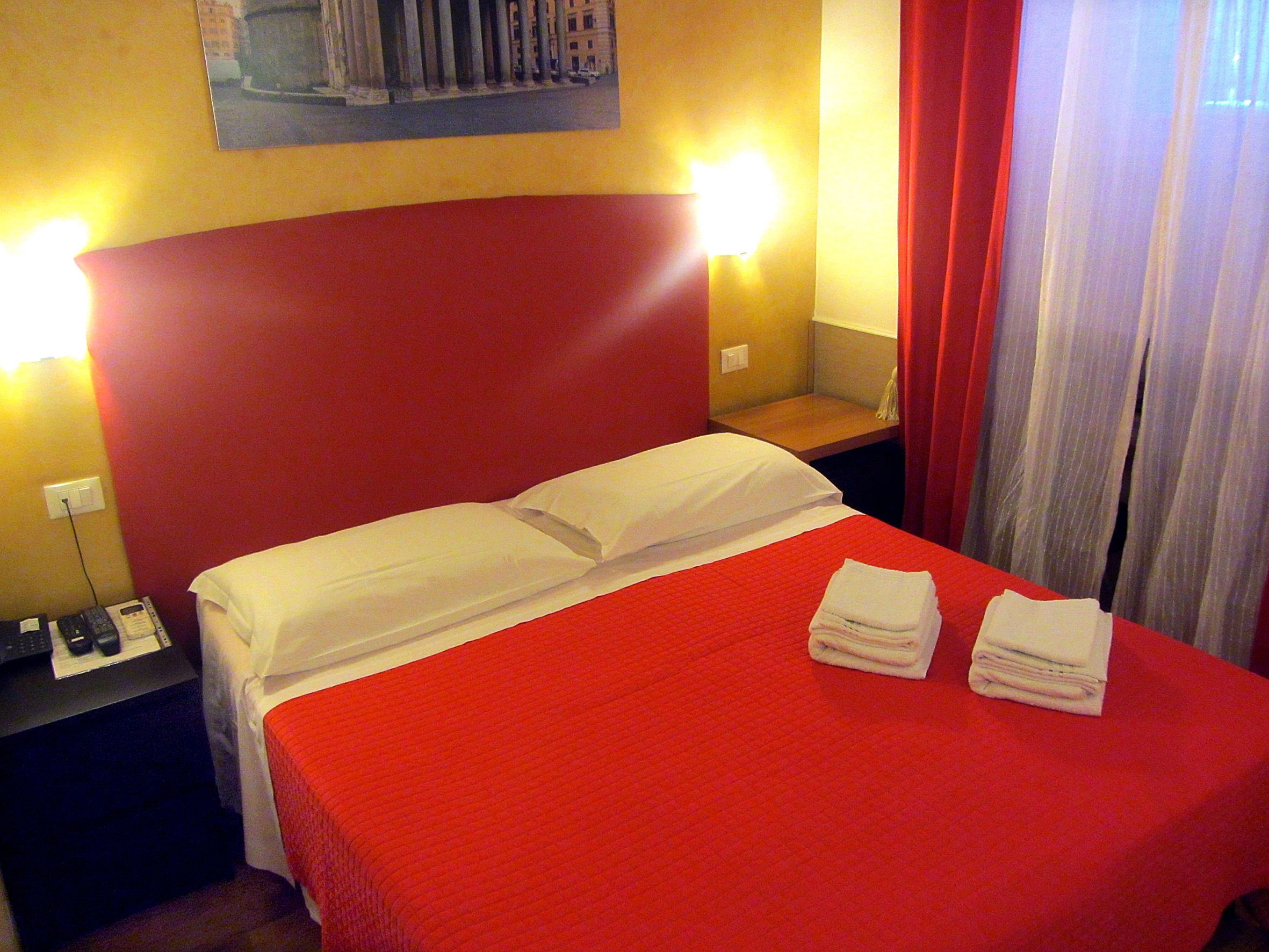 Habitació d'hotel amb estovatge vermell, almoinades blanques i un llit ben fet amb tovalloles doblades.