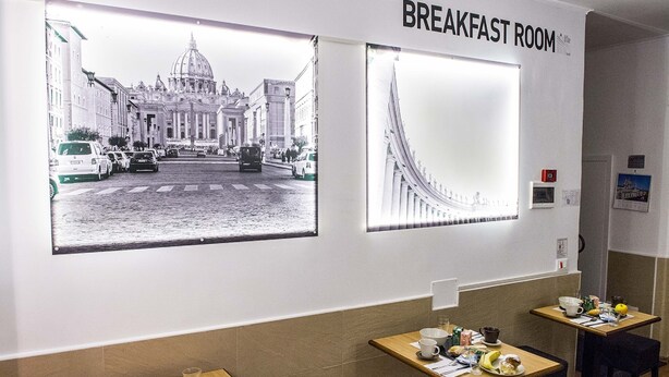 Un comedor para desayunos con dos mesas, un ventanal con vista a la ciudad y un letrero que dice "BREAKFAST ROOM".