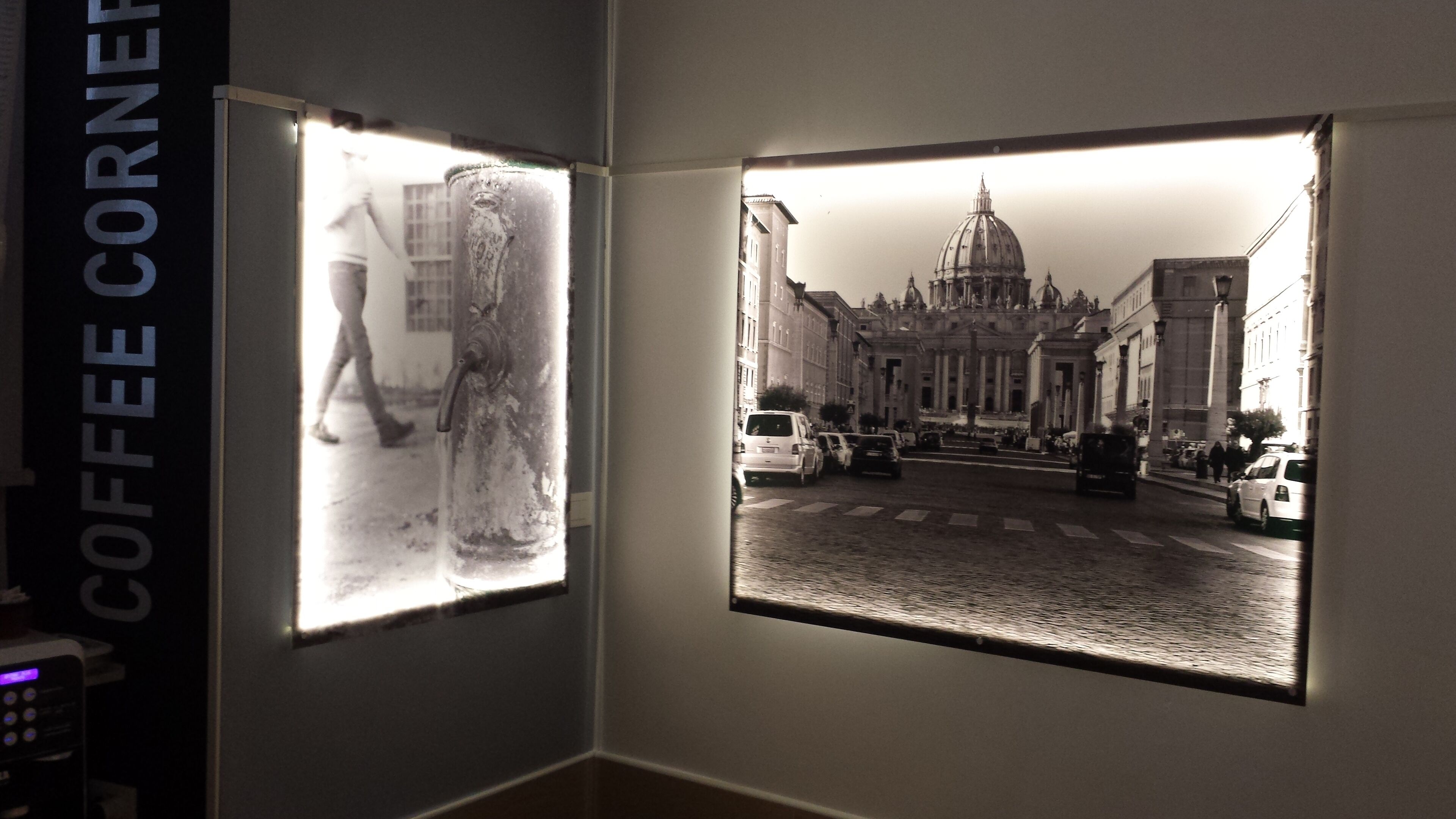 Two framed pictures on a wall, one depicting a person in a historical setting and the other showing a street with buildings and vehicles.