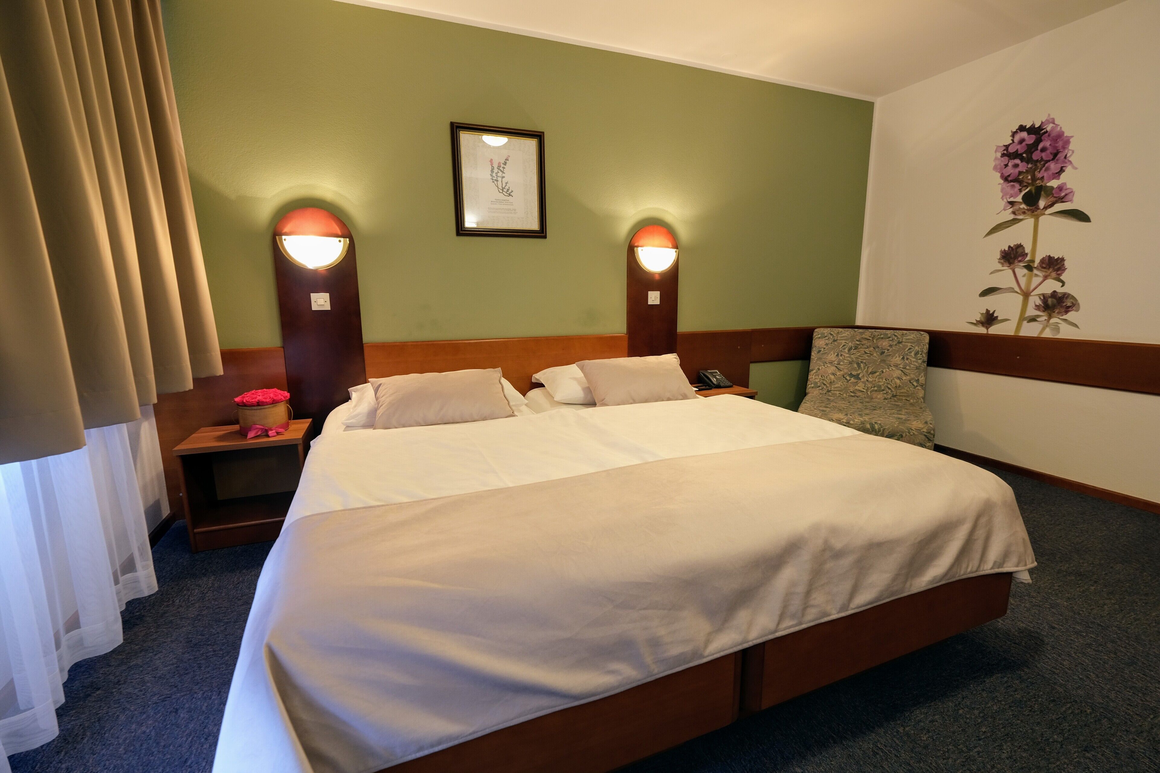 Une chambre d’hôtel avec un grand lit, deux lampes de chevet, une table de chevet et une estampe botanique encadrée au mur.