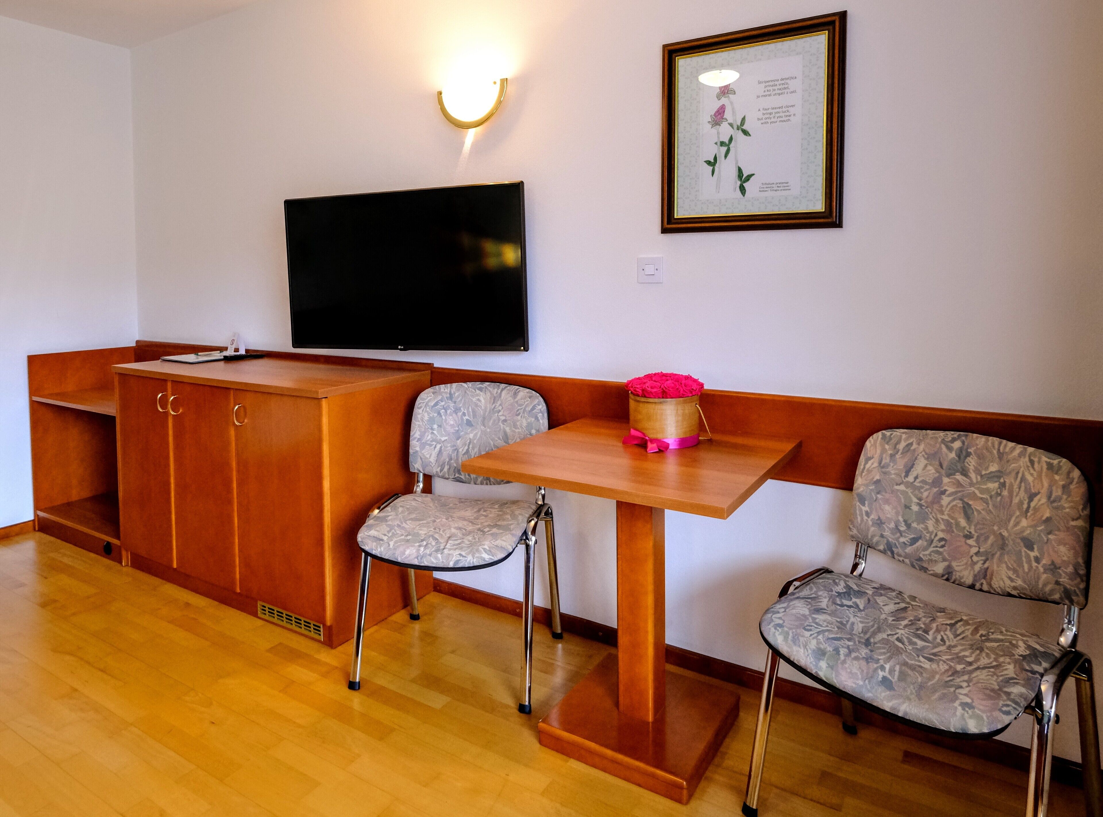 A room with a wooden desk, two chairs, a television, and a framed quote on the wall.