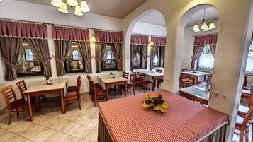 Un restaurant avec des tables et des chaises en bois, des nappes à carreaux rouges et blancs, et des rideaux marron.