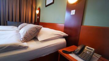 Una habitación de hotel con una cama bien hecha, una mesita de noche con teléfono y una lámpara de pared.