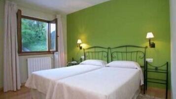 Una habitación con dos camas, una ventana con cortinas y dos lámparas fijadas a la pared.