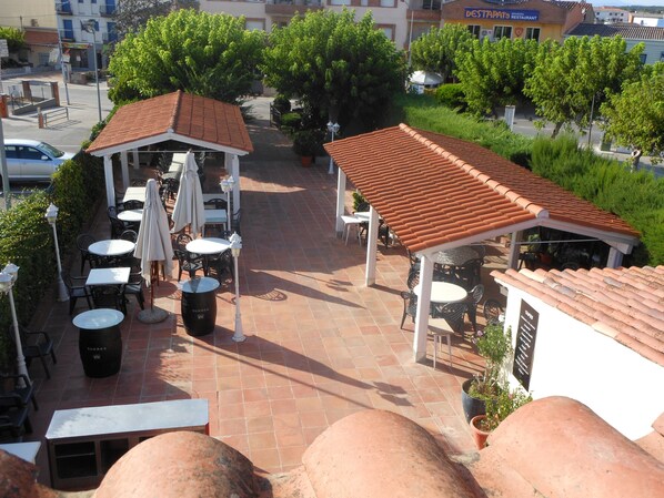Un espace extérieur aménagé en terrasse, avec des tables et des chaises, un coin salon abrité et une vue sur les bâtiments environnants.