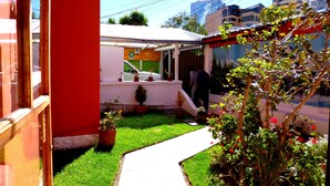 Zona exterior petita i tancada amb sostre blanc, envoltada per una paret vermella i una porta de vidre. Hi ha plantes en testos i un camí que porta a una porta.