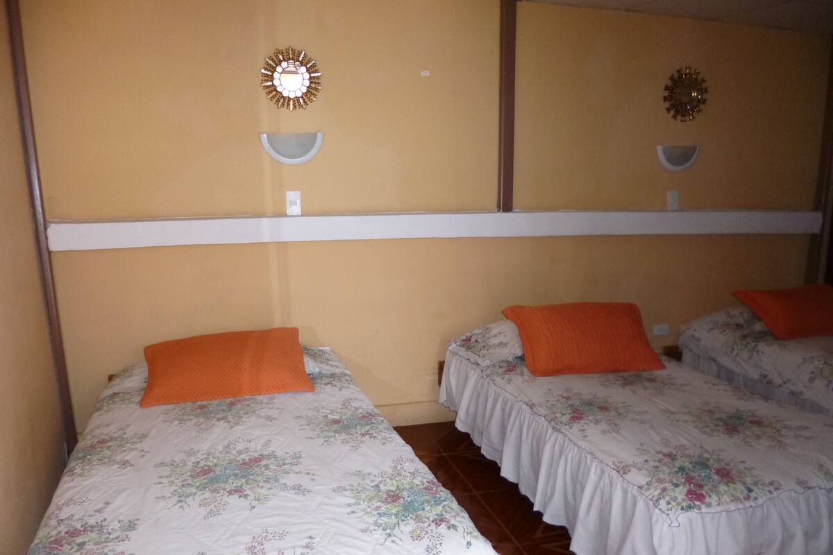 A hotel room with two single beds, each with a floral bedspread and an orange pillow.
