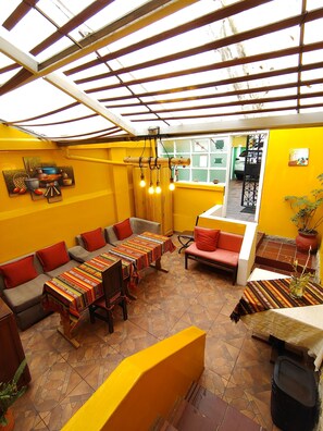 Une terrasse ensoleillée aux murs jaunes, dotée d’un plafond en bois et d’un coin repas avec une table et des chaises.
