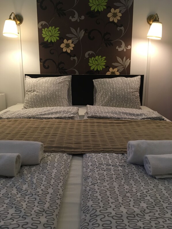 A hotel room with a large bed, two bedside lamps, floral wallpaper, and neatly folded towels. - Europa Centerpoint Guesthouse (Budapest)