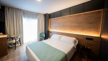 A modern hotel room with a large bed, a desk, a chair, and a wooden headboard.